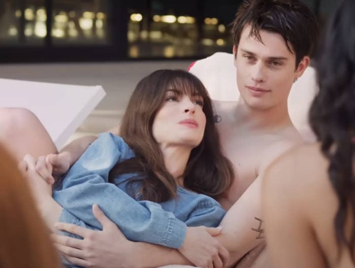 Anne Hathaway and  Nicholas Galitzine in The Idea of You lounging outside as they talk to others
