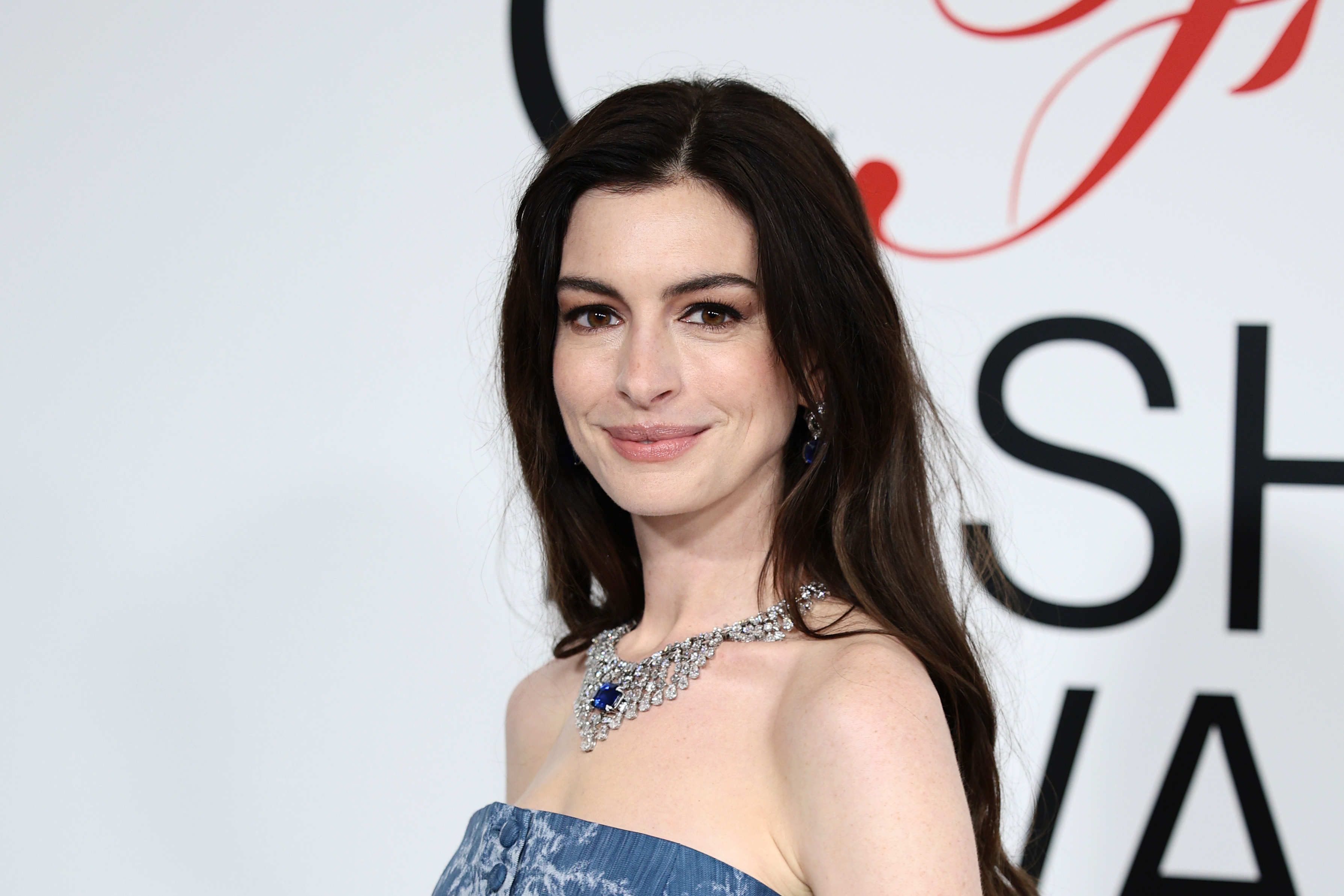 Anne Hathaway wearing an off-shoulder gown with a sparkling necklace, posing at an event