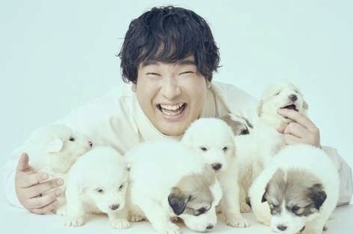 笑顔の男性が白い子犬に囲まれています。背景には「FIGHT CLUB OKAZAKI TAIKU」と記されています。