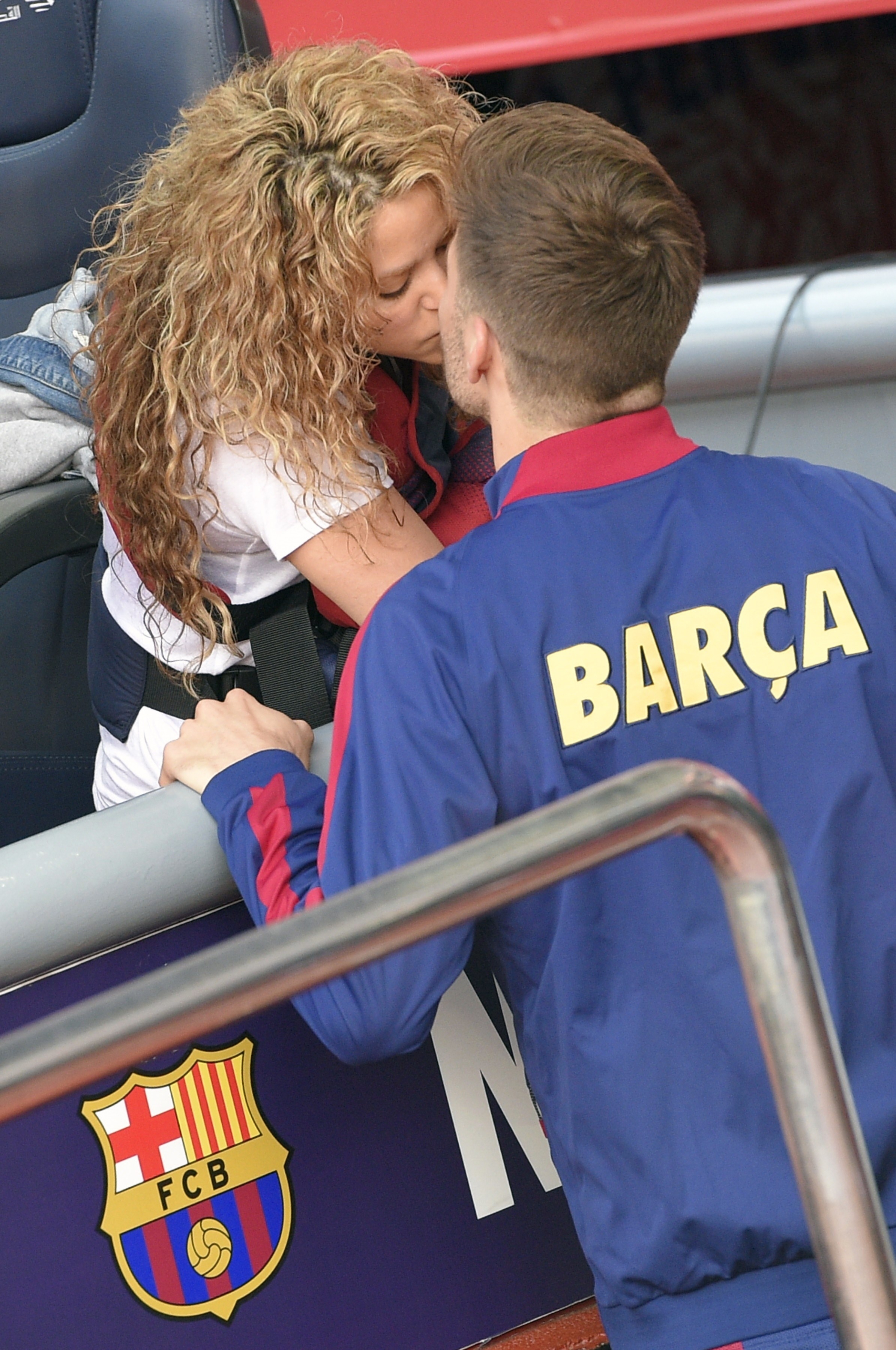 Shakira and Gerard Piqué share a kiss, Shakira in a sleeveless top and Piqué in a BARCA jacket