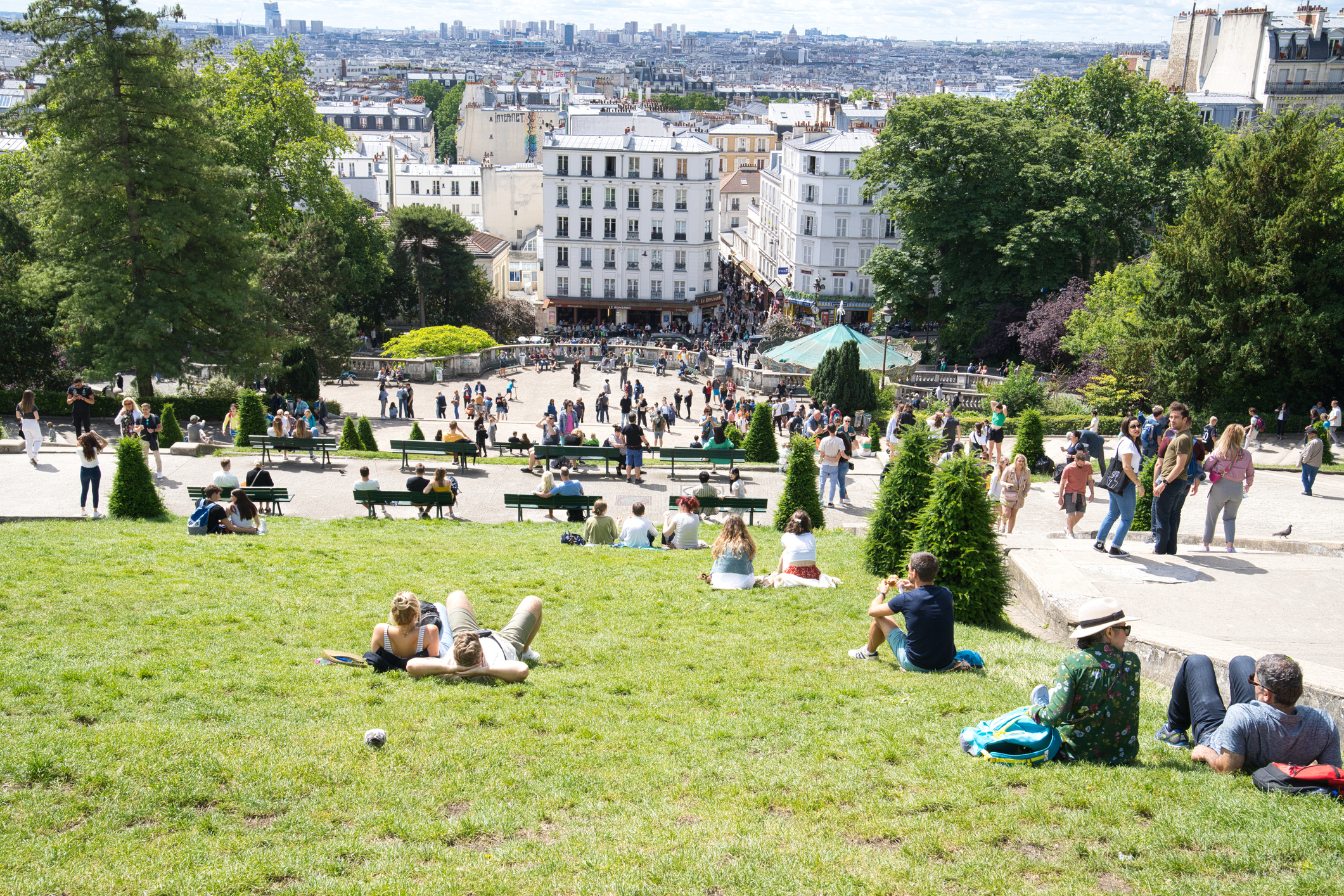 People relaxing and walking in a busy park with benches and a central staircase on a sunny day