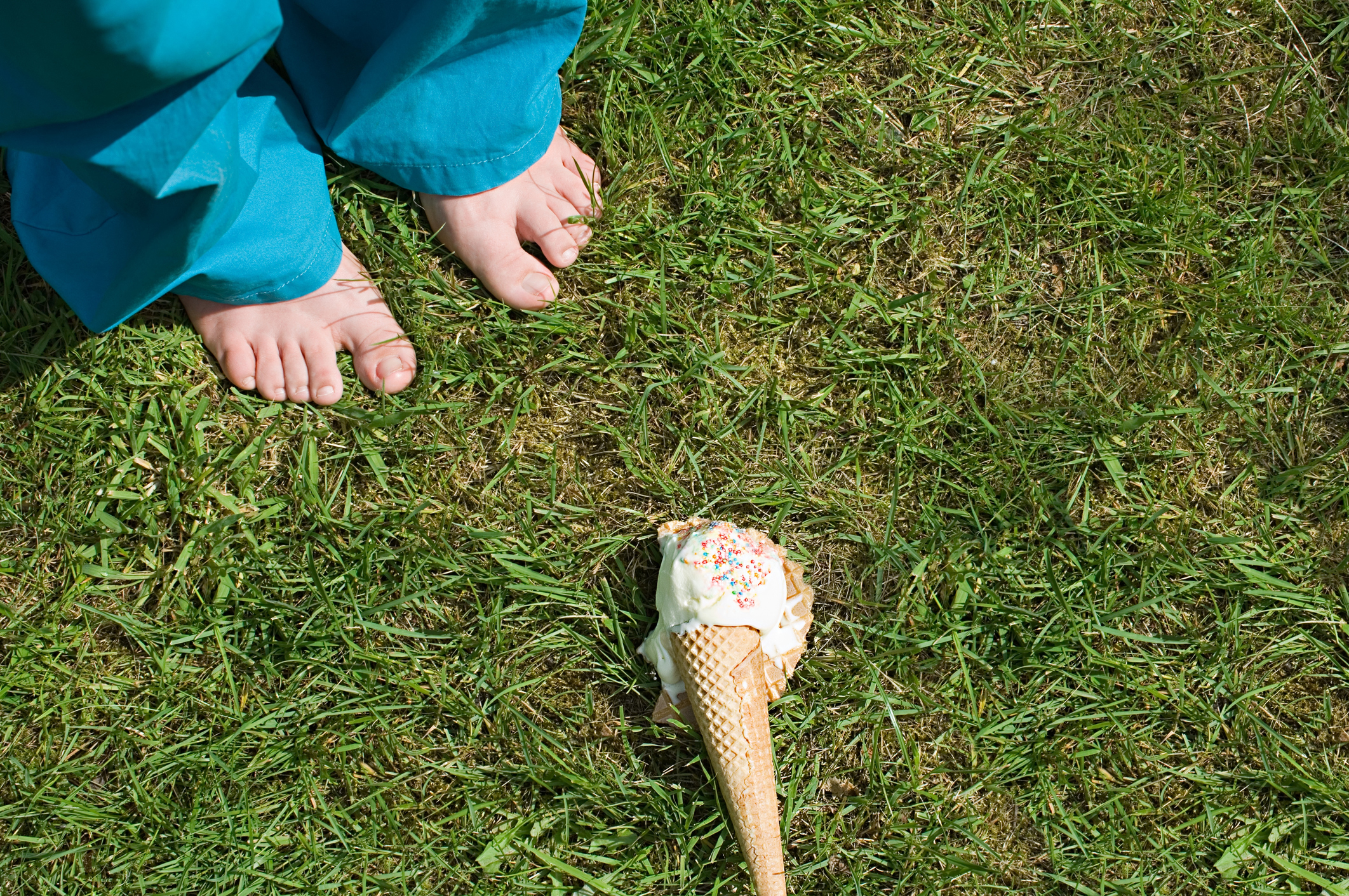 Bare feet next to a dropped ice cream cone on grass, conveying a sense of a small mishap or loss