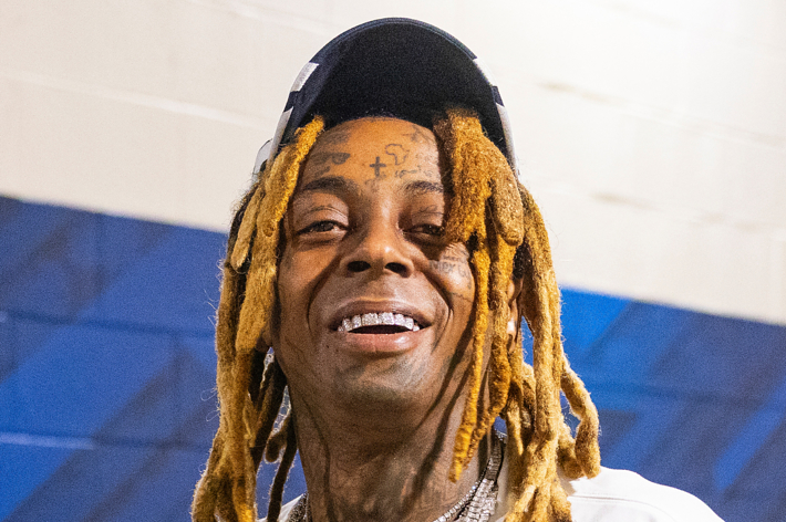 Lil Wayne in a casual shirt, smiling, with distinctive tattoos on his face