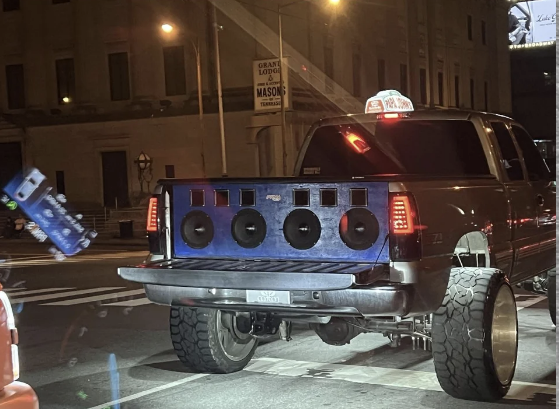 Truck with oversized wheels and large speakers in the bed stopped on a city street at night