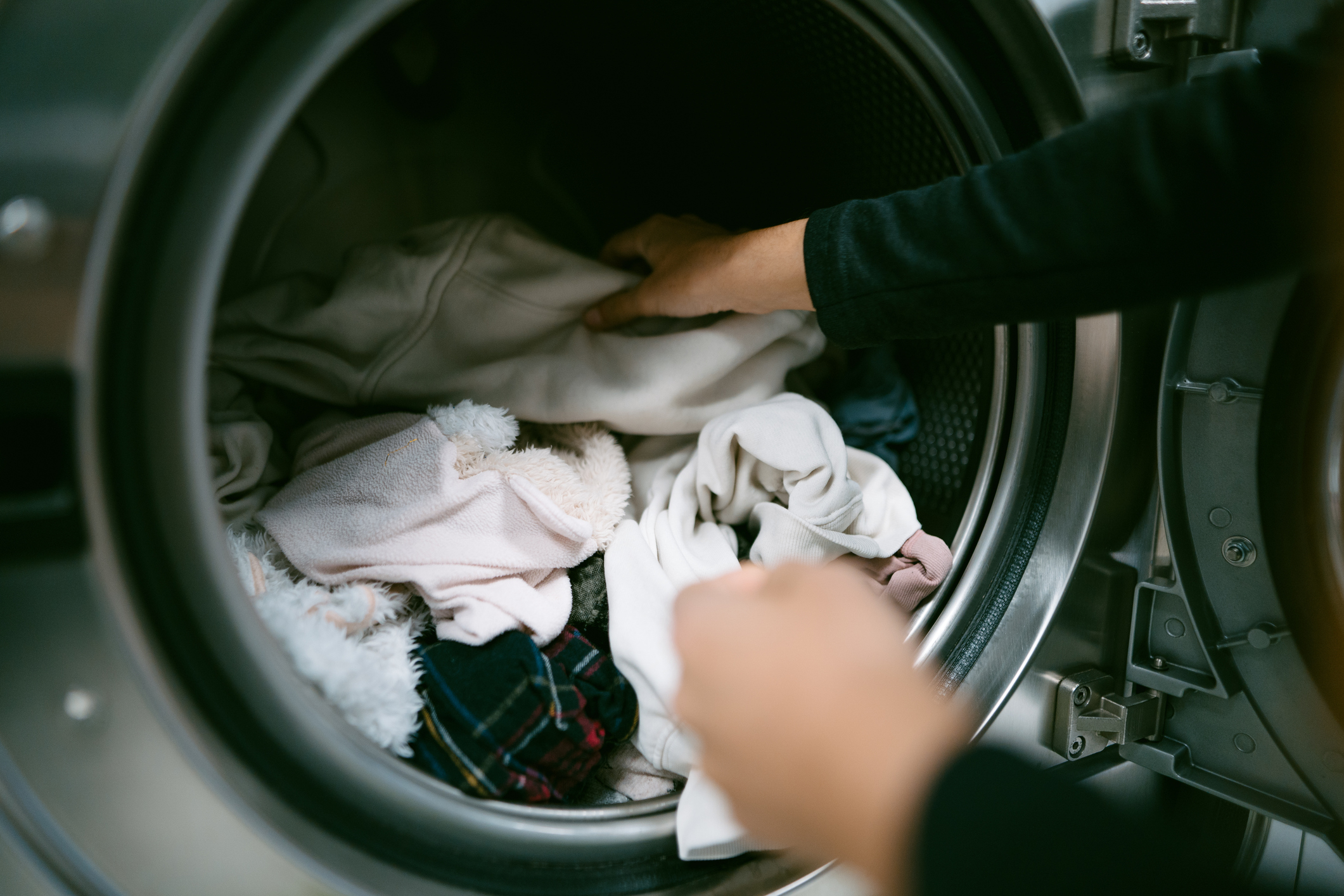 Person&#x27;s hands placing laundry into a washing machine