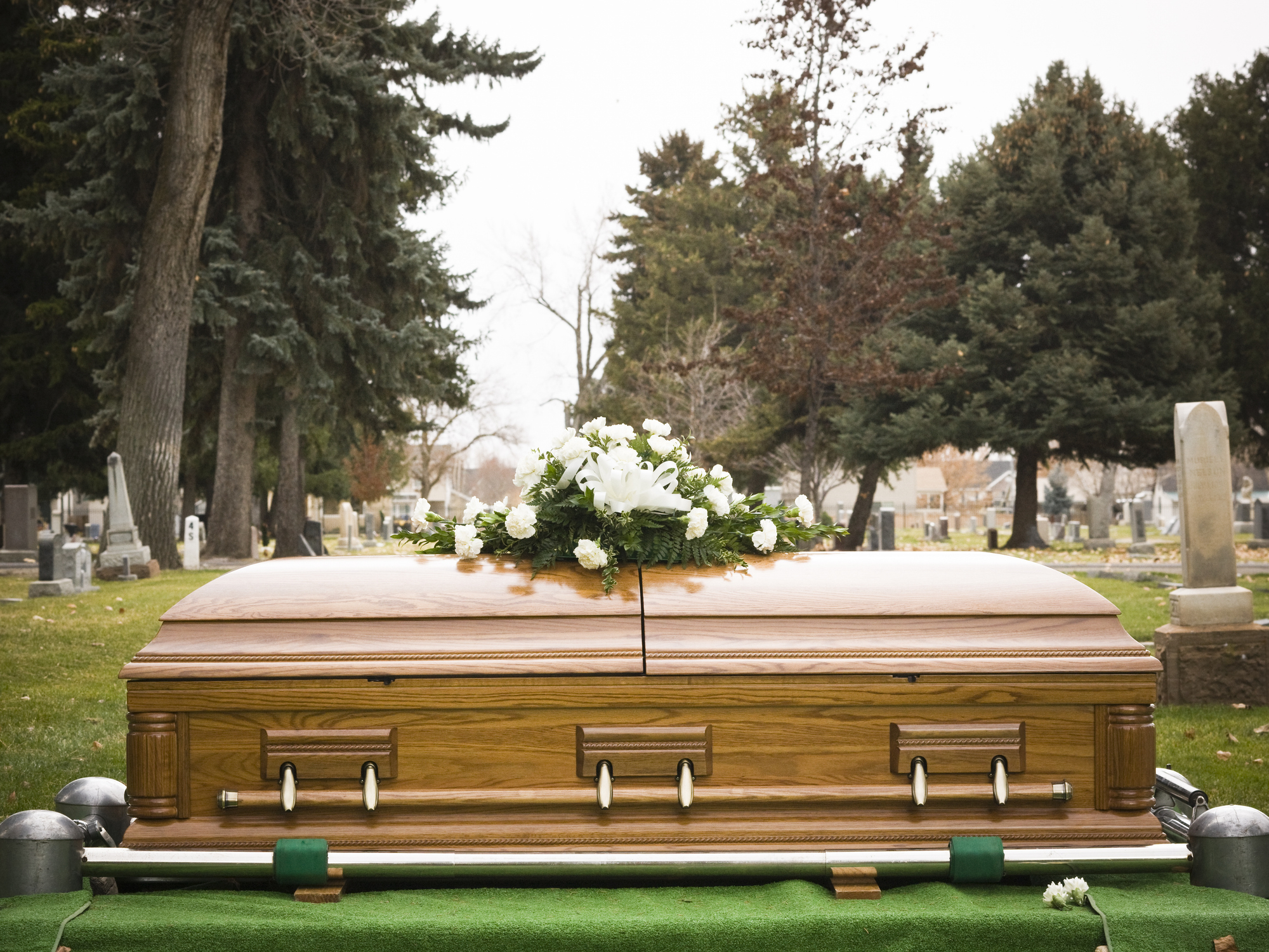 Wooden casket with white flowers on top at a cemetery setting