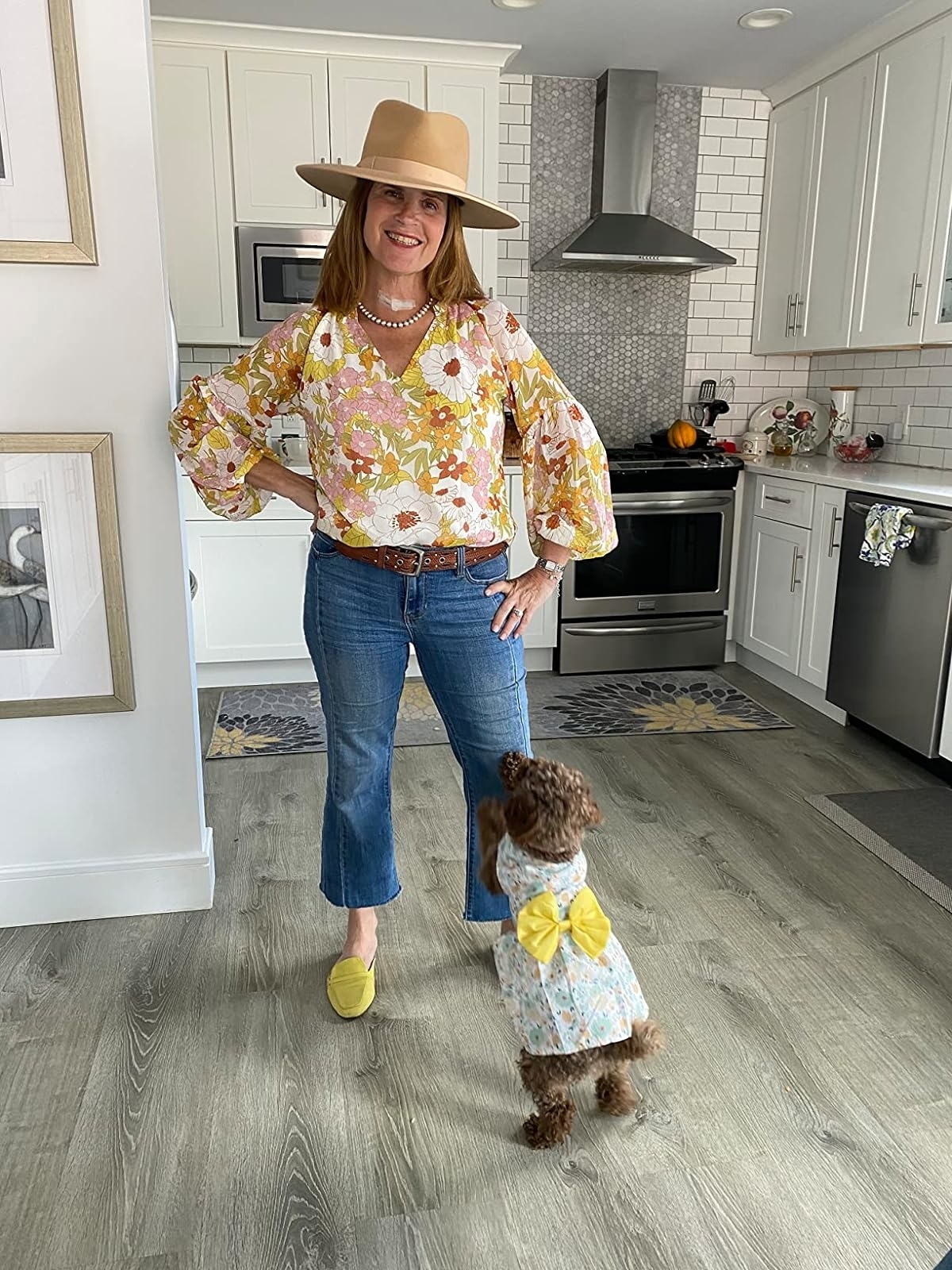Reviewer in floral blouse and jeans with hat, dog dressed in matching outfit beside her in kitchen