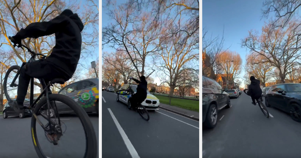 Person on bike popping a wheelie on a street with parked cars and bare trees in the background