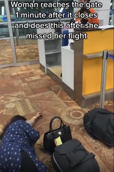 Woman lies on airport floor, upset for missing her flight, with luggage nearby