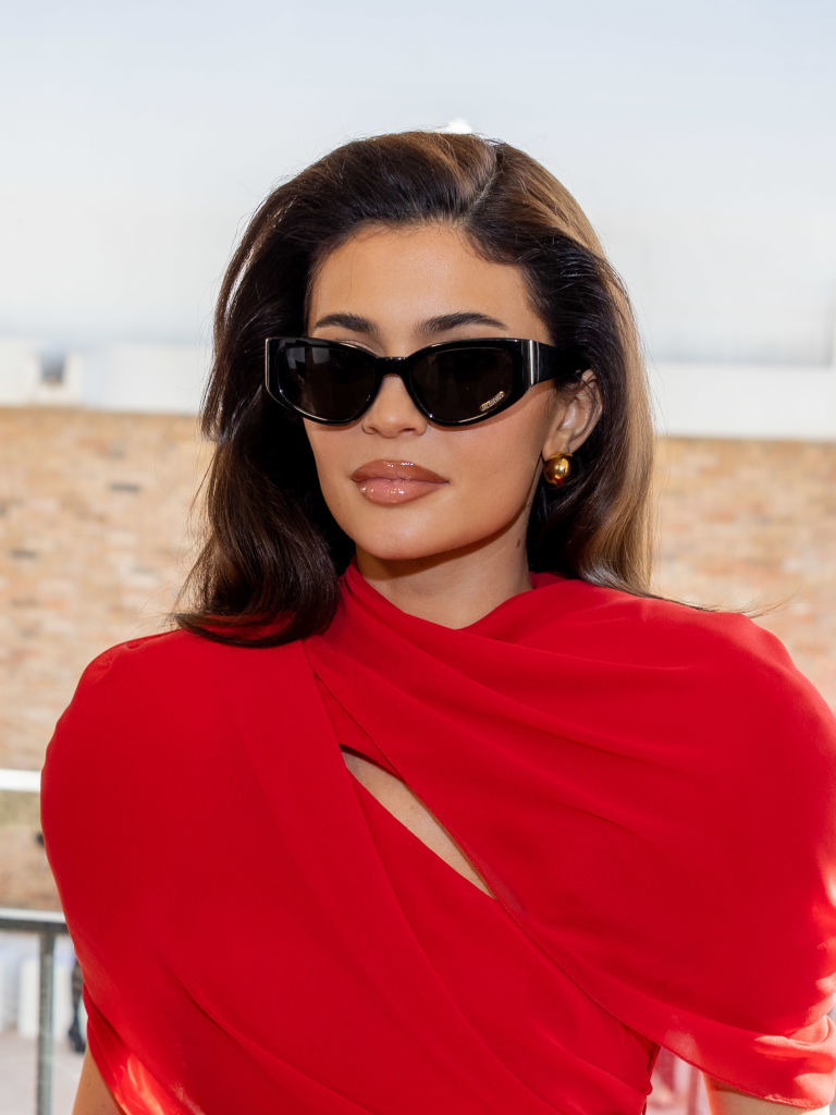 Kylie in a stylish red dress with unique shoulder cutouts and large sunglasses posing for a photo