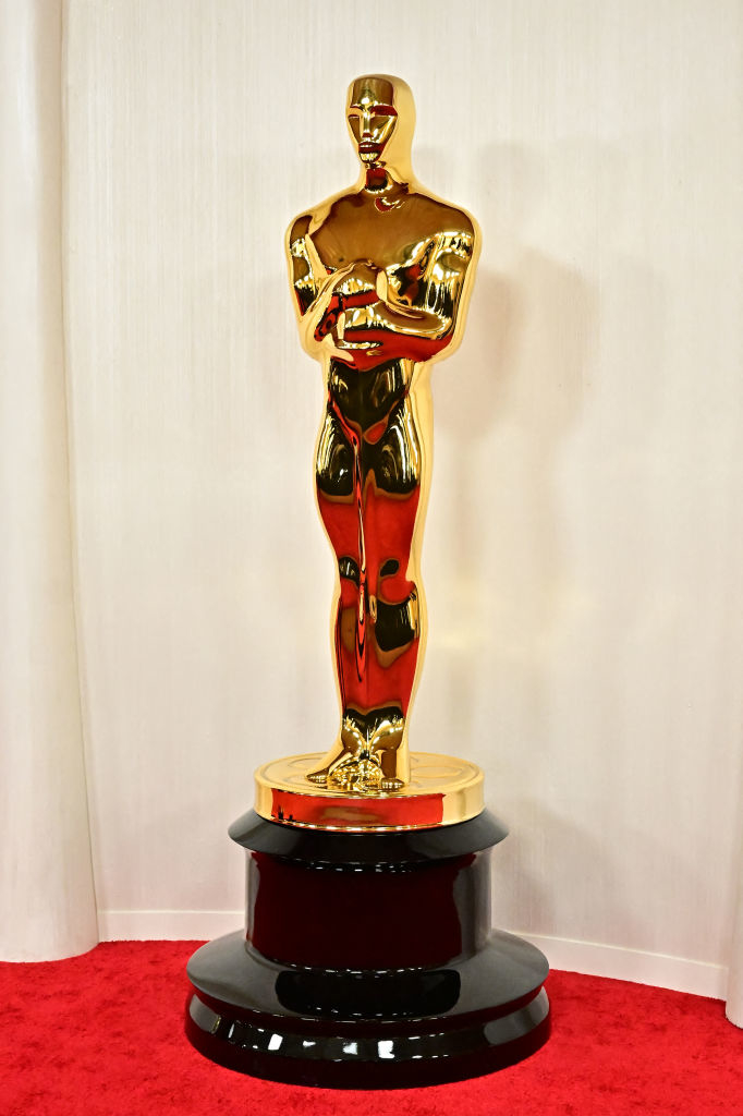 Photo of the Oscar statuette against a plain background, positioned on a pedestal with a red carpet beneath it