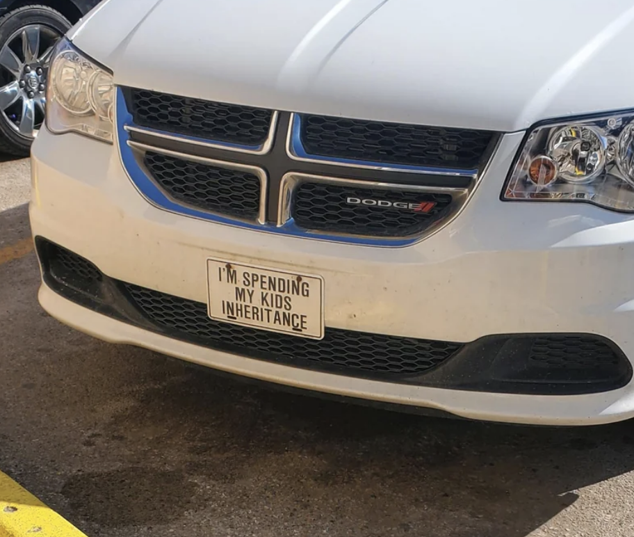 Front of a car with a license plate frame reading &quot;I&#x27;M SPENDING MY KIDS&#x27; INHERITANCE&quot;