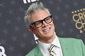 Man in a green suit and glasses smiling at a camera on the red carpet