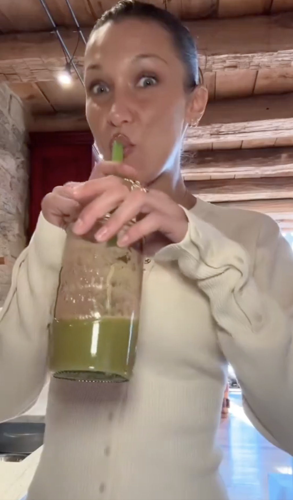 Bella sipping a green drink through a straw, wearing a casual buttoned top