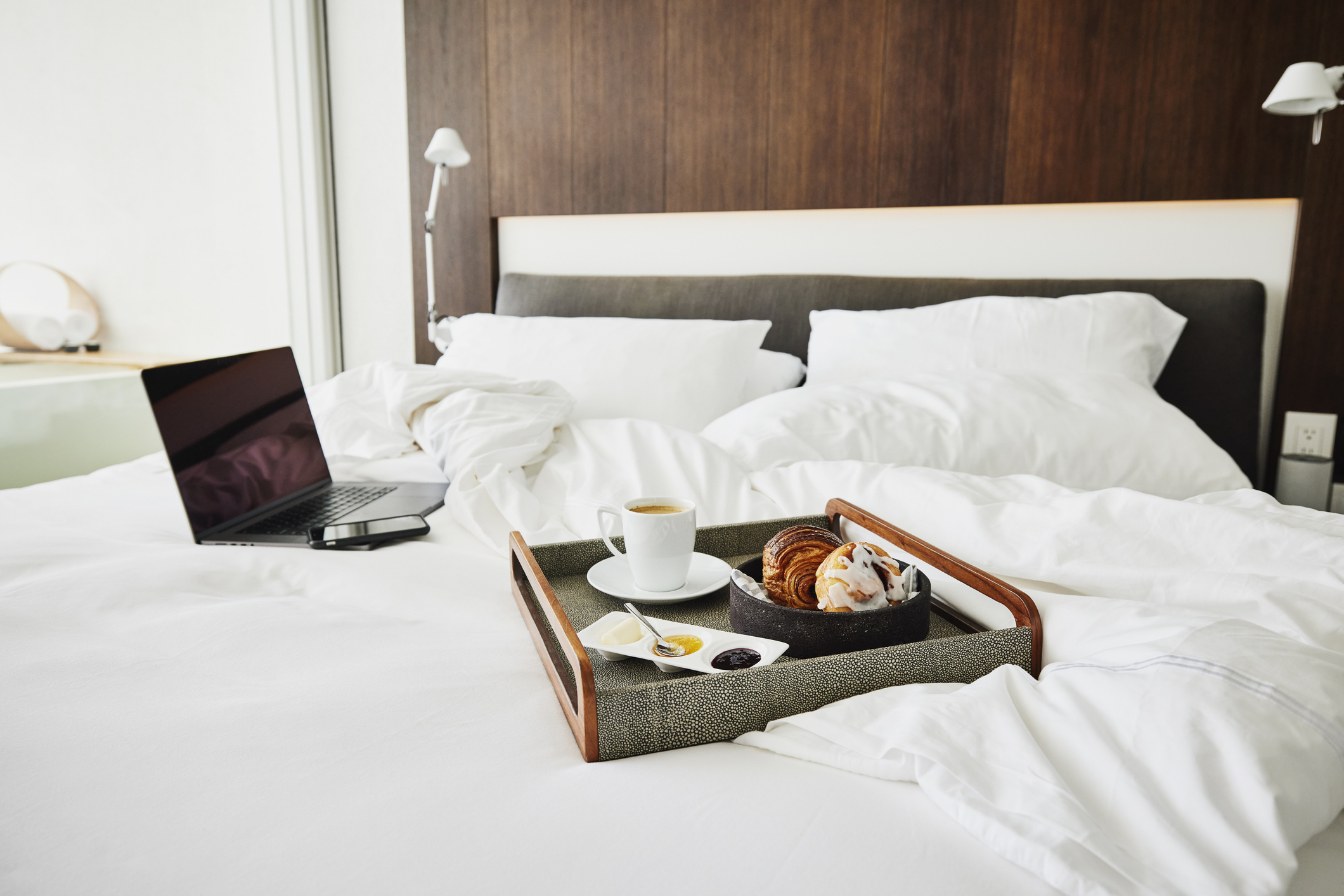 Breakfast on tray with laptop on bed in a modern room, suggesting working during a leisurely morning
