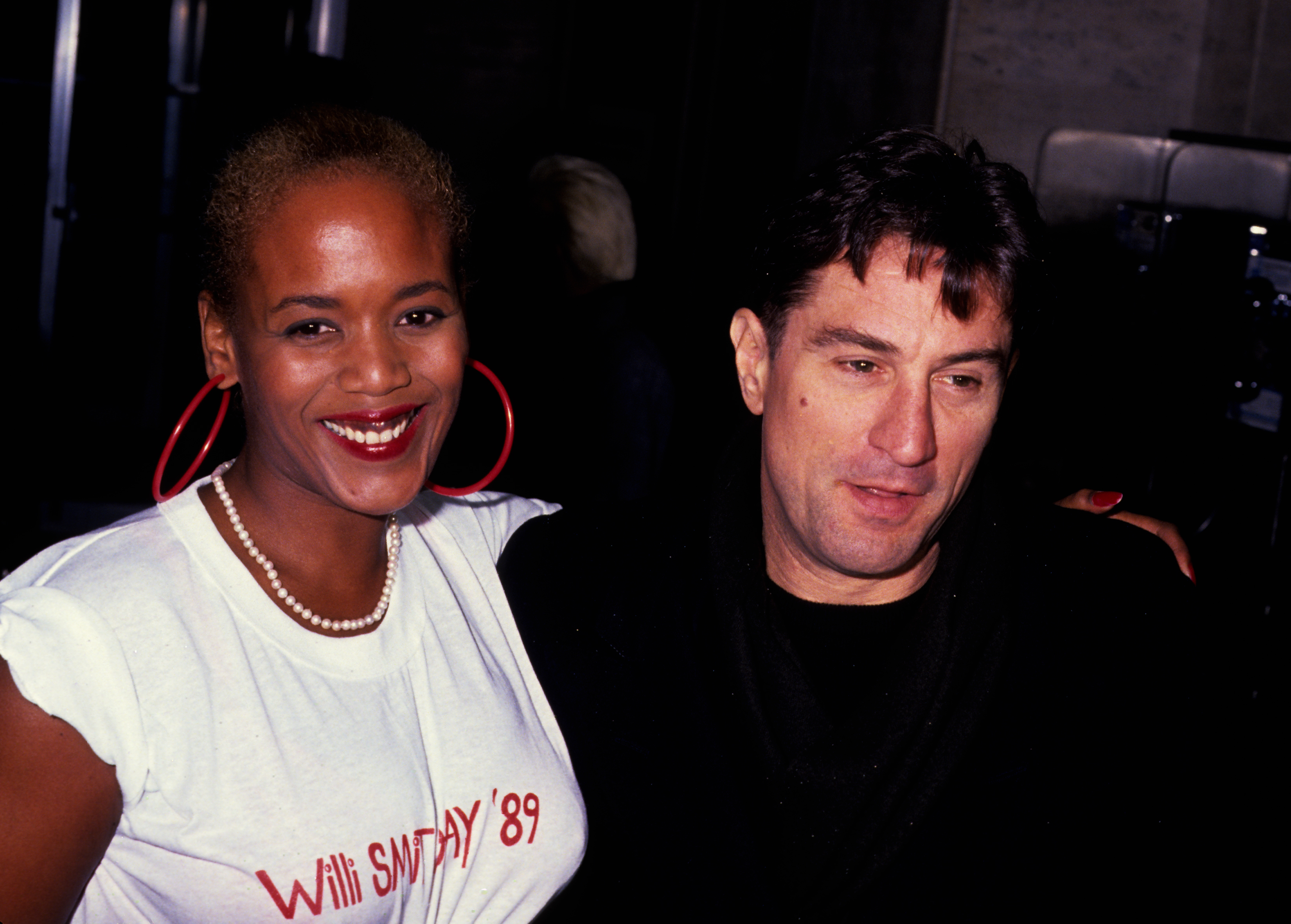 Toukie Smith in a graphic tee and De Niro in a dark jacket, both smiling