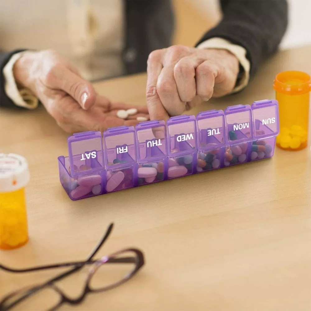 Hands organizing medication into a labeled weekly pill organizer on a table