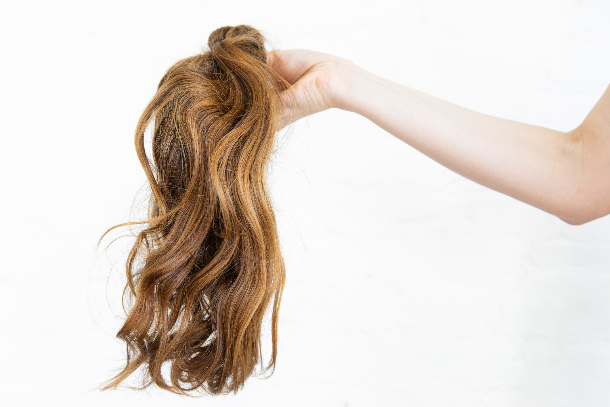 Hand holding a wavy hair extensions piece against a white background