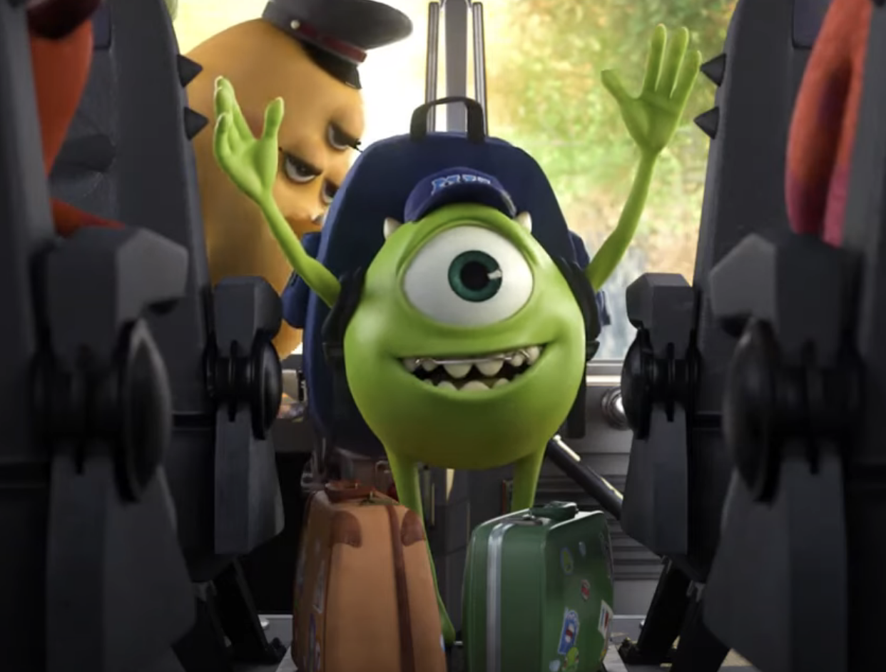 Mike Wazowski is smiling in a bus seat with Sulley visible behind him, both from Monsters, Inc