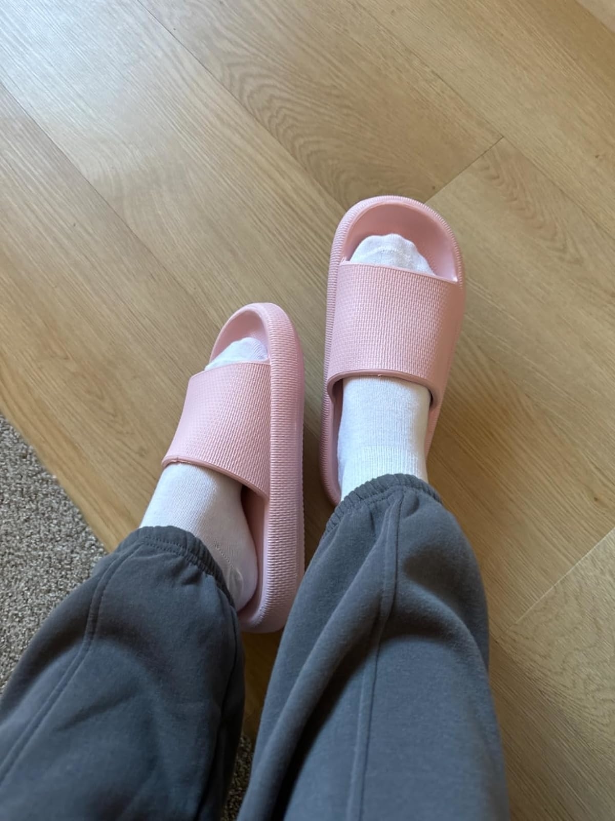 Person wearing white socks with pink slide sandals and grey sweatpants, highlighting comfortable indoor wear