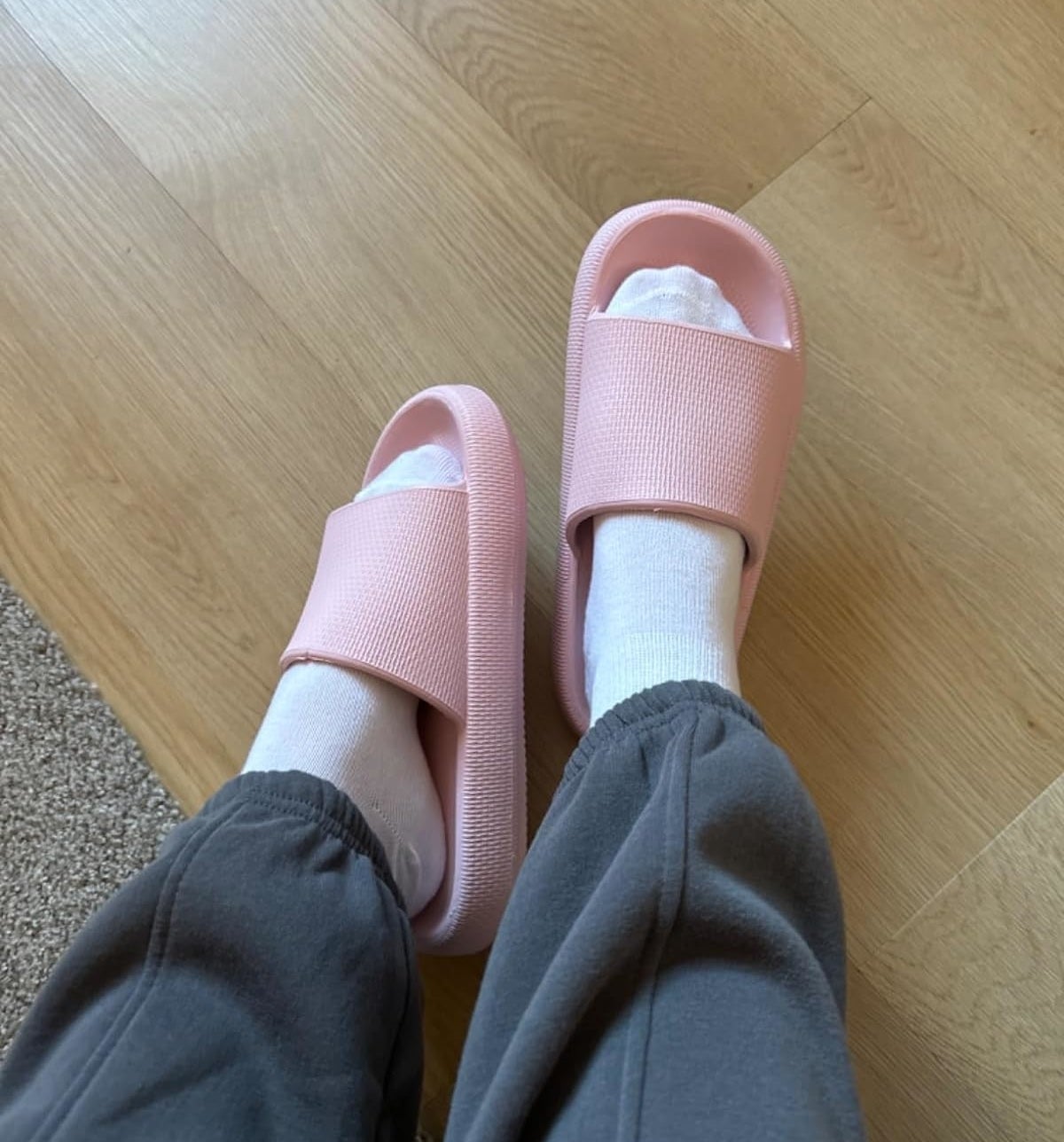 Person wearing white socks with pink slide sandals and grey sweatpants, highlighting comfortable indoor wear