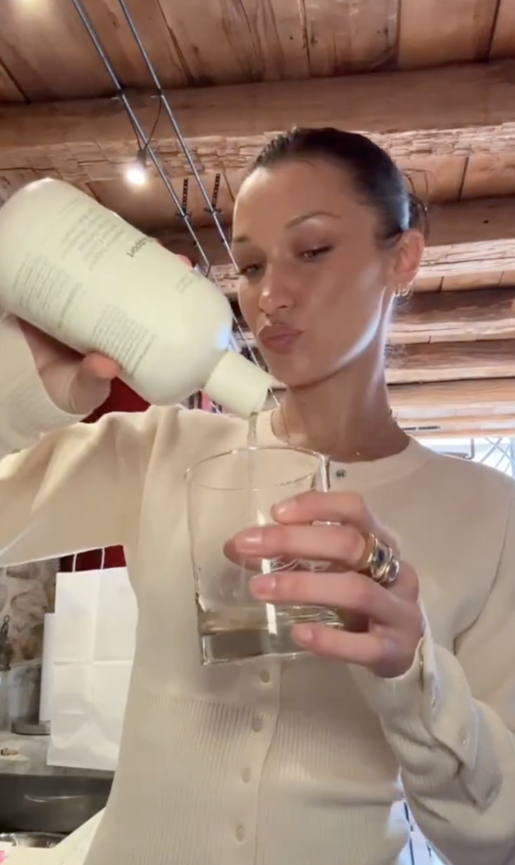 Bella Hadid pouring from a bottle into a glass with her lips pursed