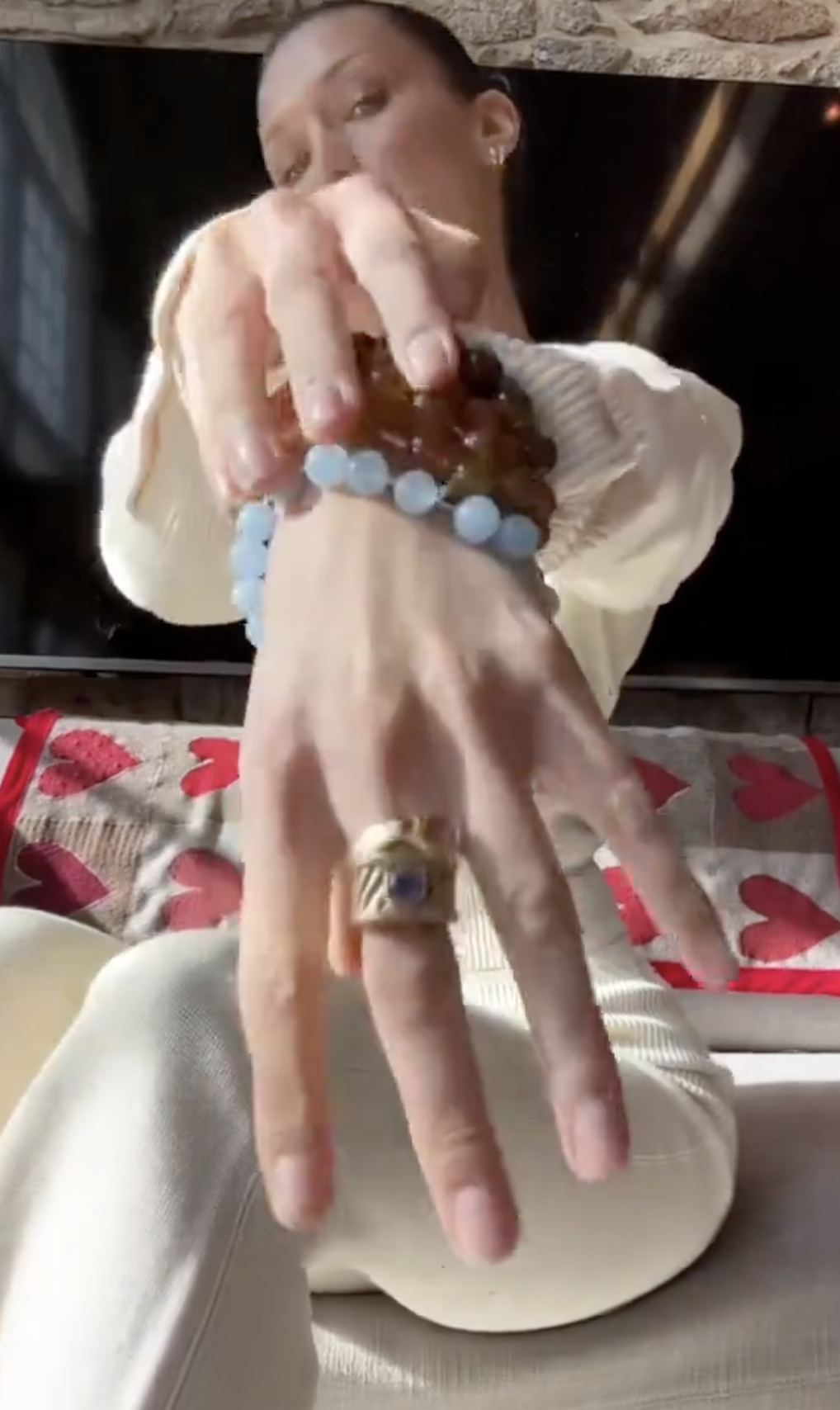 Bella in a white shirt and cream pants puts on various bracelets and a ring