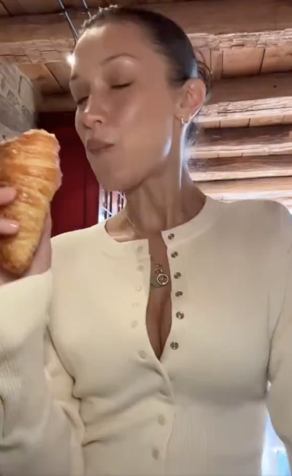 Bella in a buttoned top holding a croissant with eyes closed