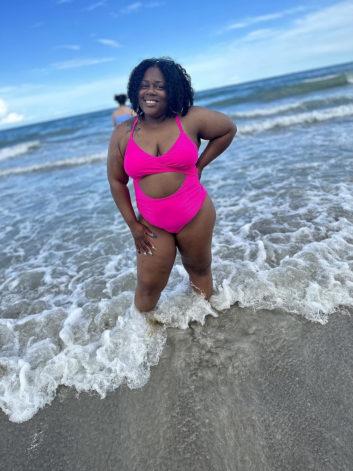 Model in a pink two-piece swimsuit standing on a beach with waves around her feet