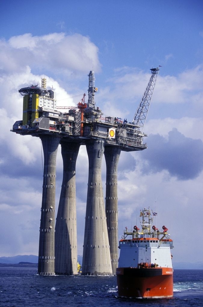 Offshore drilling platform rising far above the ocean on four towers, with a supply ship nearby