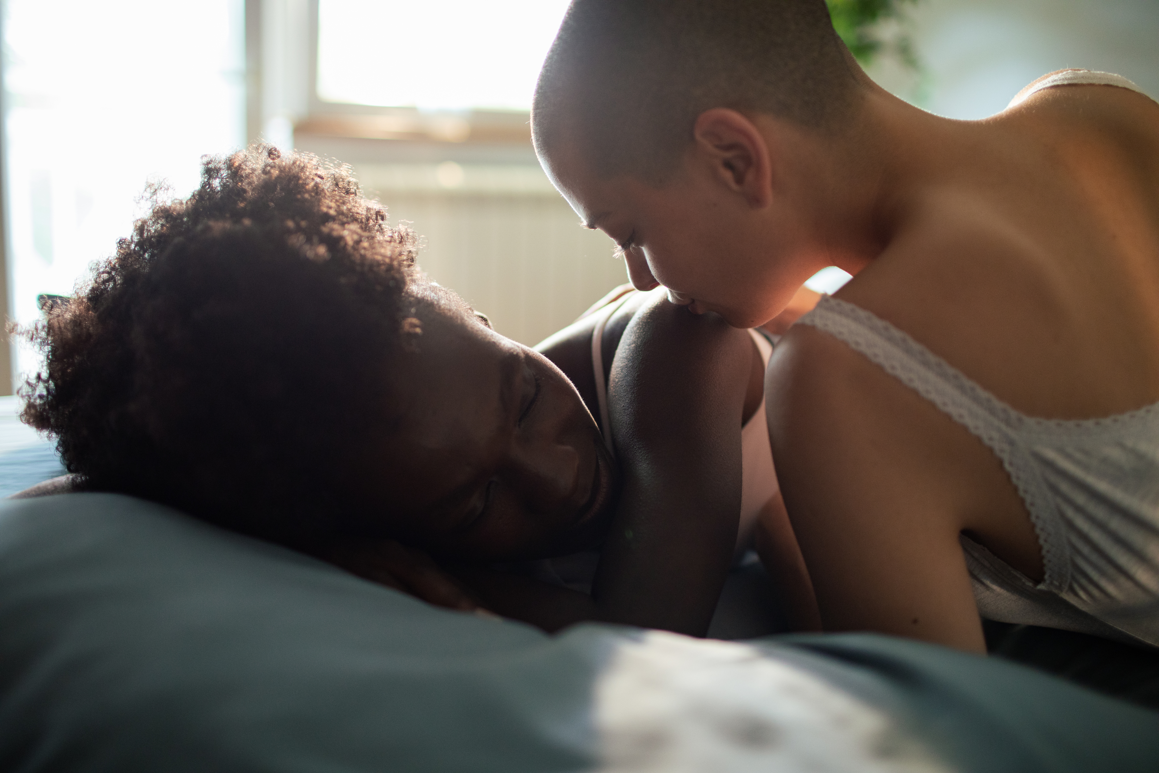 Two people share an intimate moment, one lying in bed and the other leaning over, foreheads touching