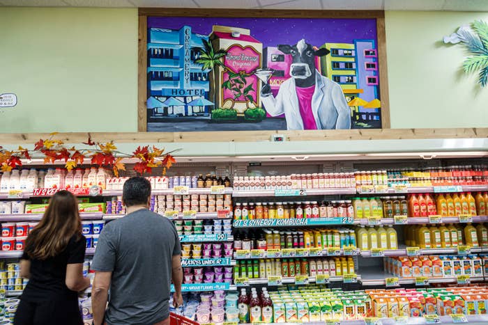 Two people shopping in a grocery store aisle facing a colorful mural above the shelves