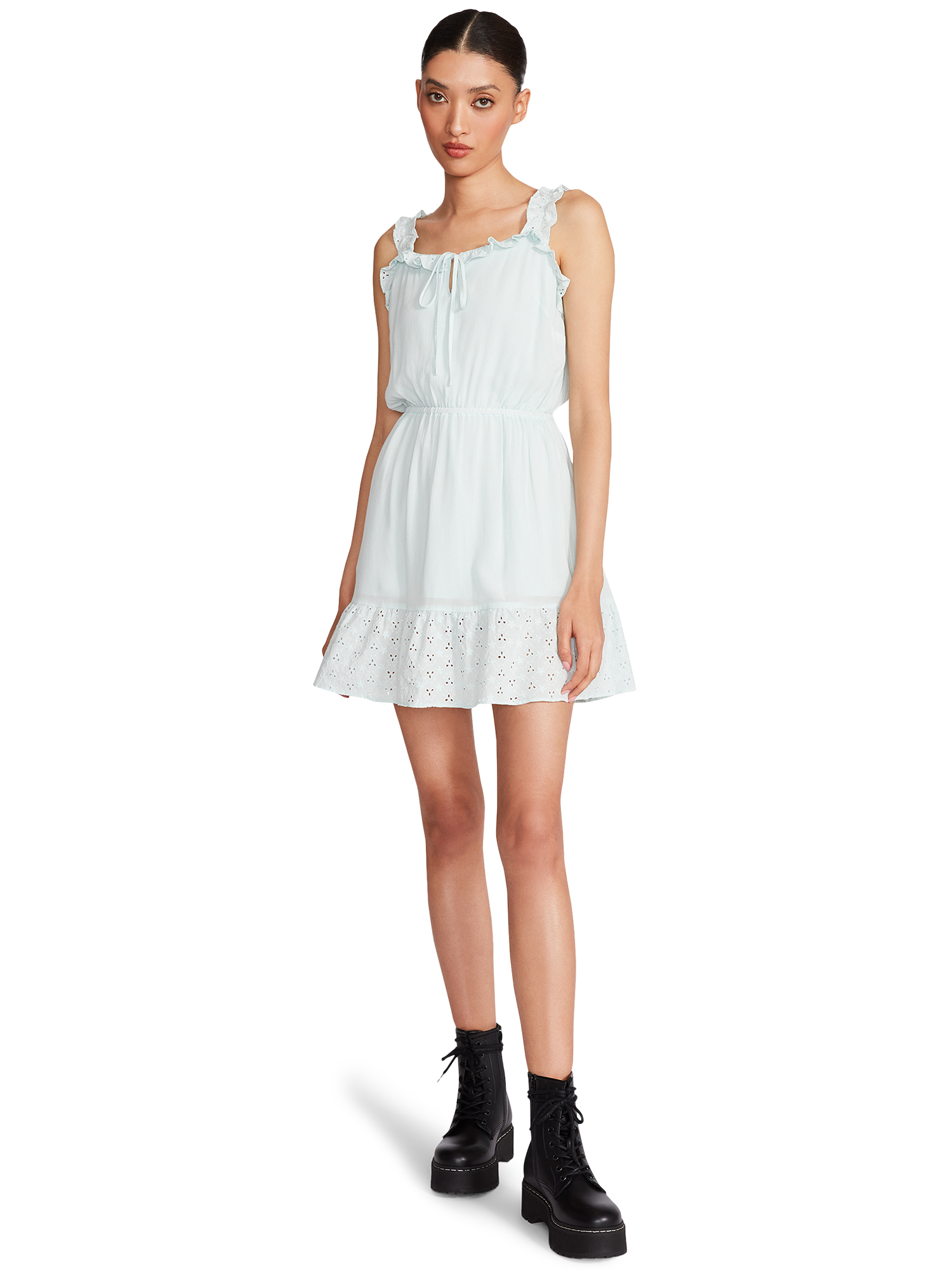 A model poses in a sleeveless mini dress with eyelet hem detail, paired with black boots