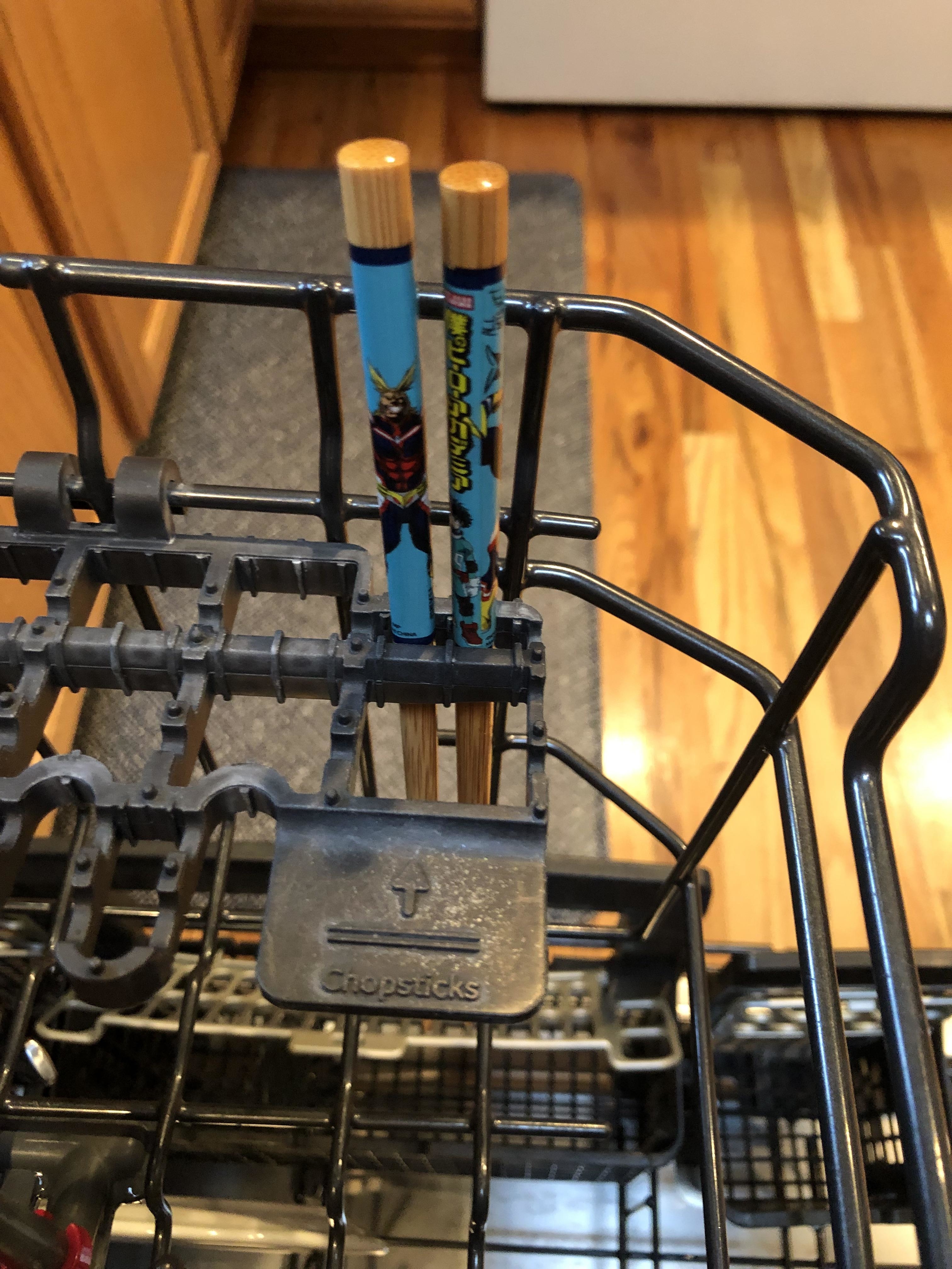 Two decorative chopsticks held upright in a dishwasher utensil rack for cleaning