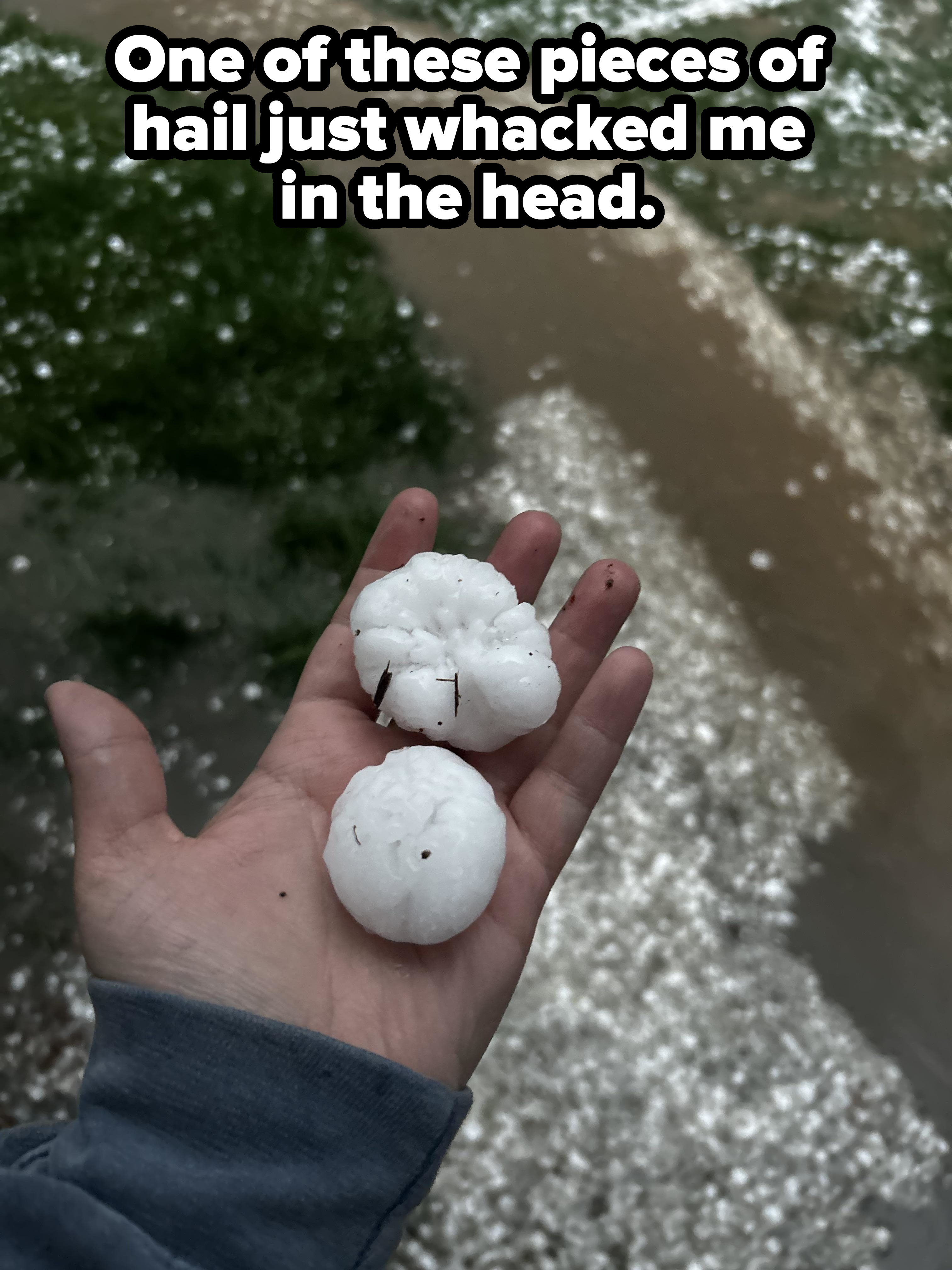 Person holds three large hailstones in their hand with a grassy area and pathway in the background