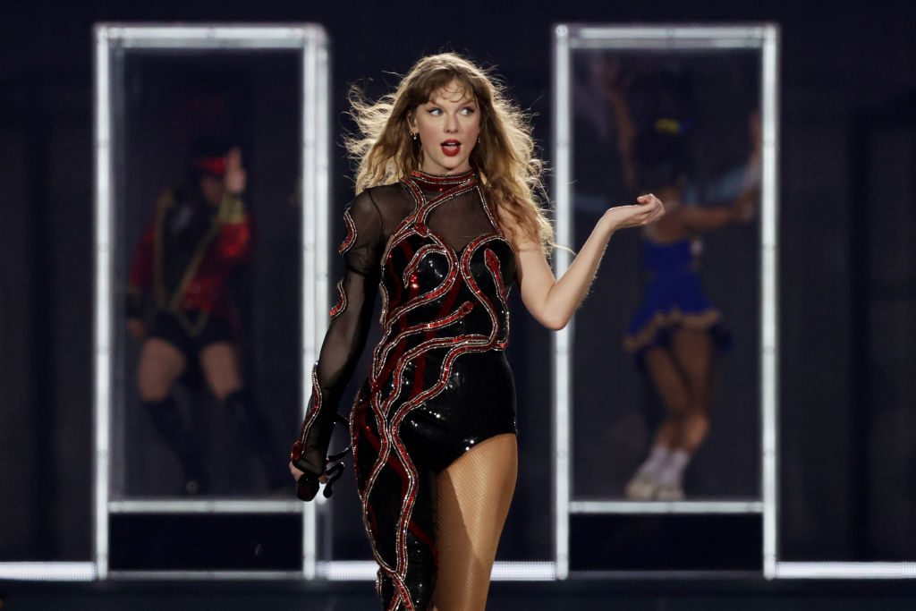 Taylor Swift in a stage performance wearing a sequined bodysuit with sheer elements, engaging with the audience