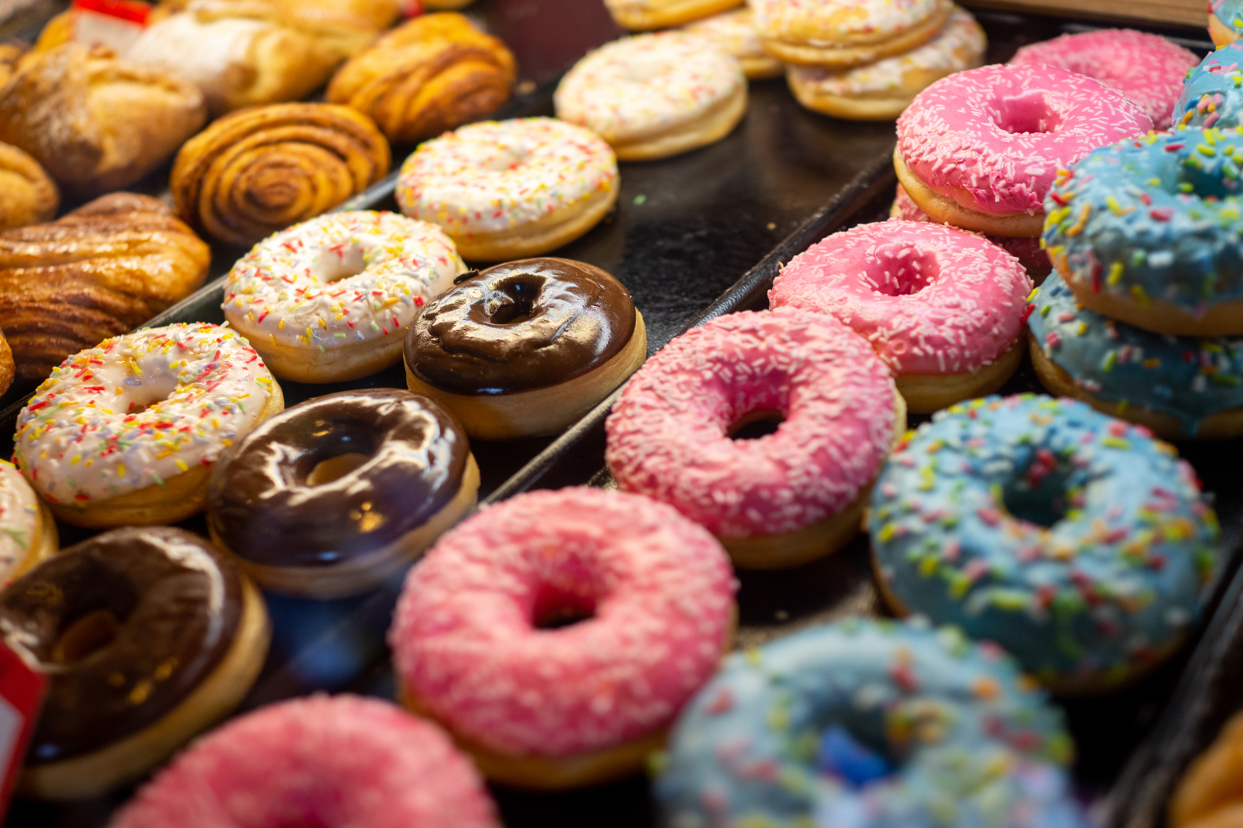 Assorted doughnuts on display, including glazed, chocolate, and sprinkled varieties