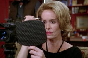Sarah Paulson looking in a mirror to draw on her eyebrows.