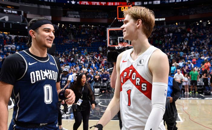 Two basketball players from opposing teams are having a friendly chat on the court post-game