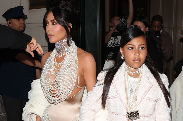 Kim Kardashian in a layered pearl necklace and matching white outfit with her daughter North West in a white jacket and layered necklaces