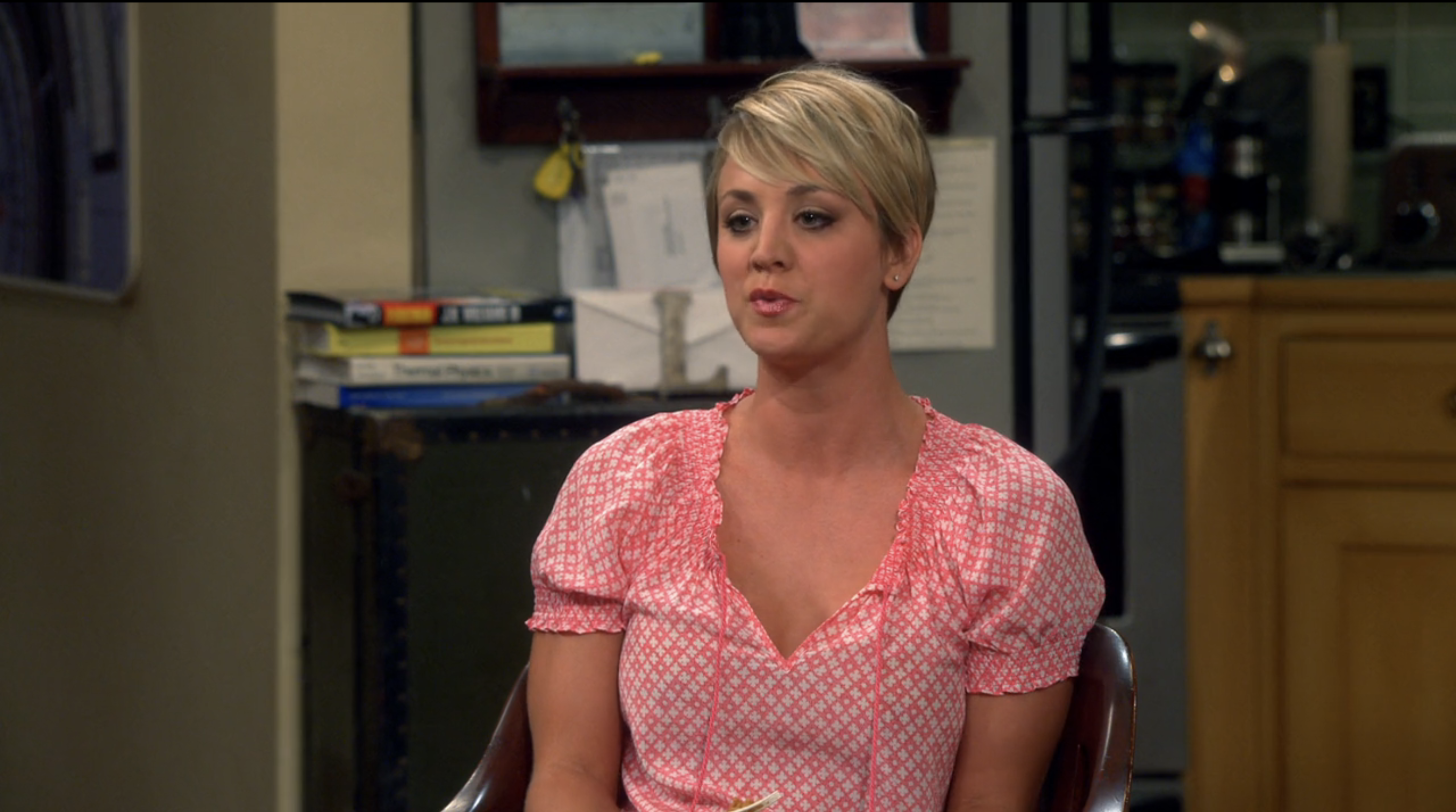 Woman in pink polka dot blouse and short hair sitting in a living room, from a TV show