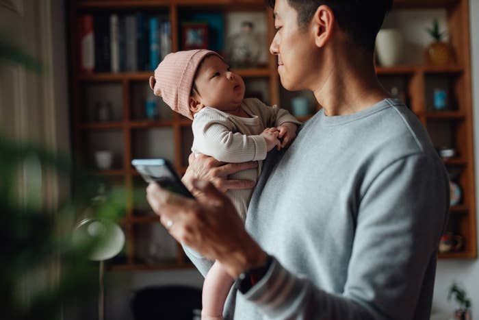 Adult holding a baby looking at each other, while the adult is also holding a smartphone