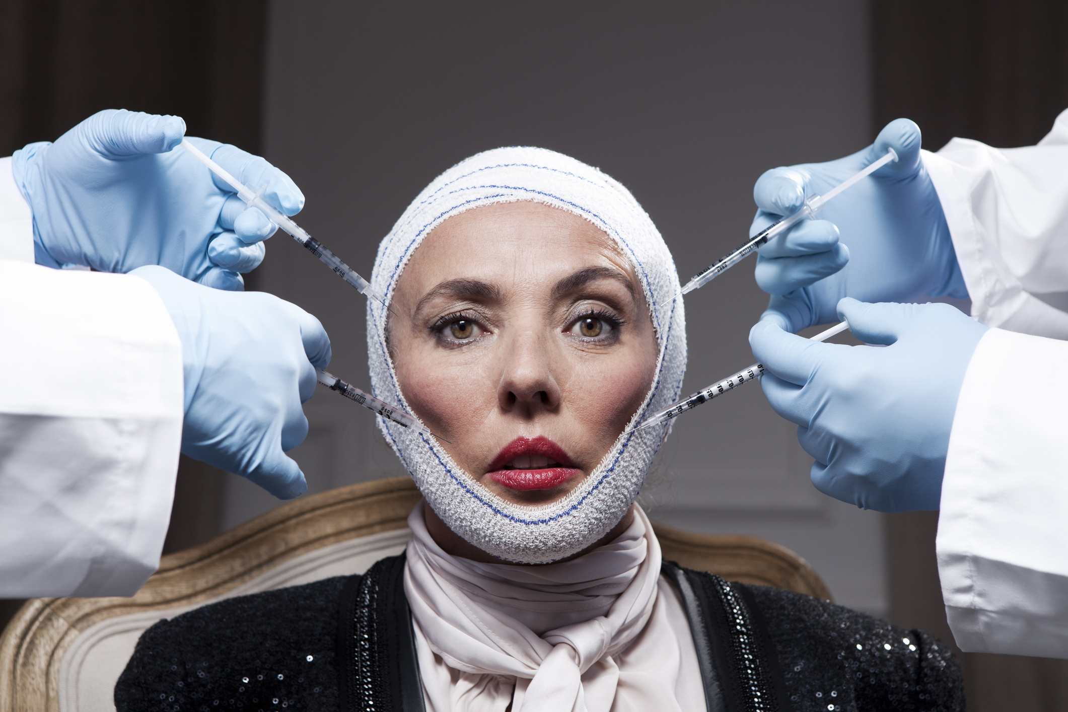 Woman with bandaged head surrounded by hands with medical tools, post-cosmetic procedure look