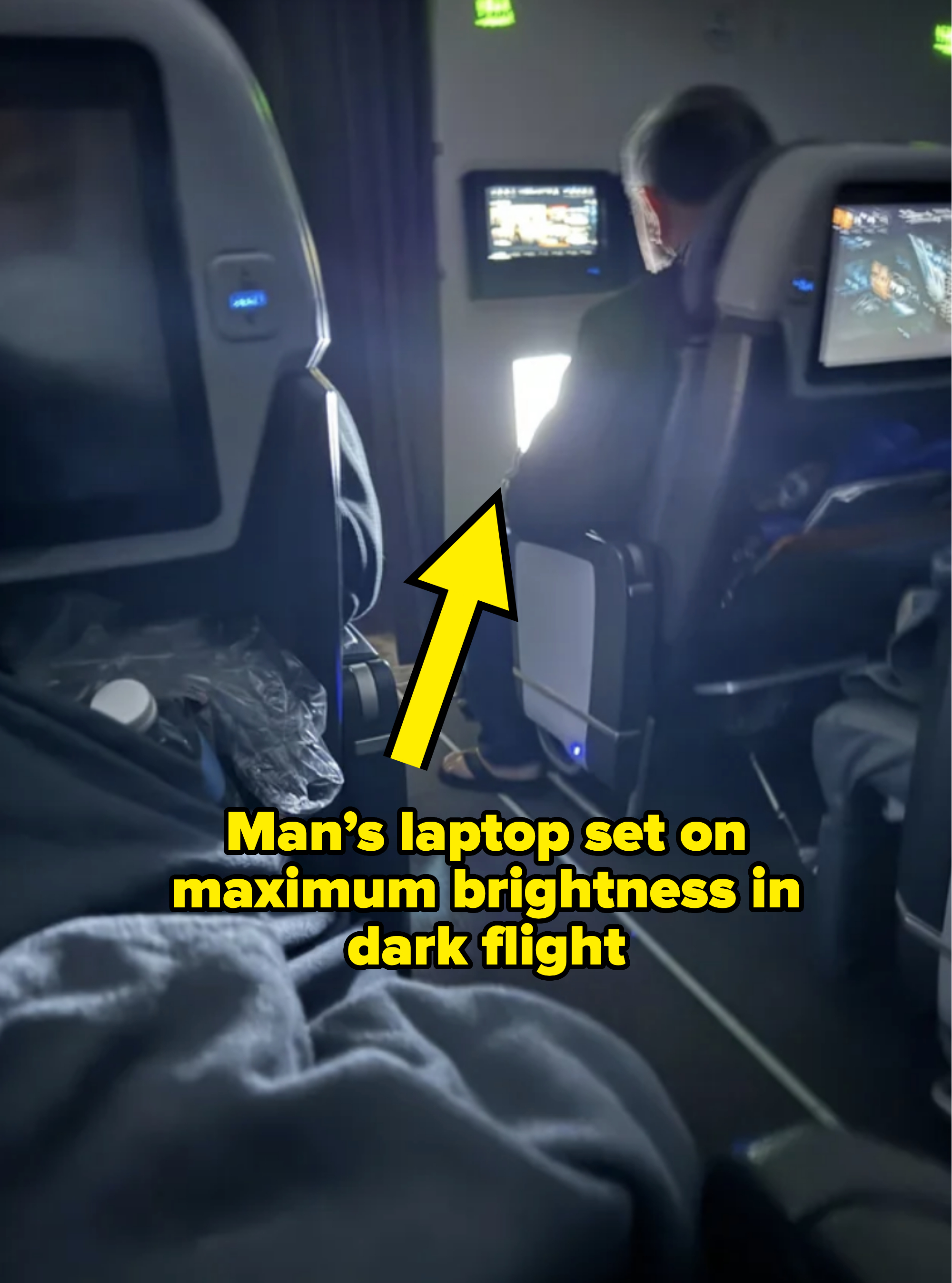 a man with his laptop on bright during a dark flight