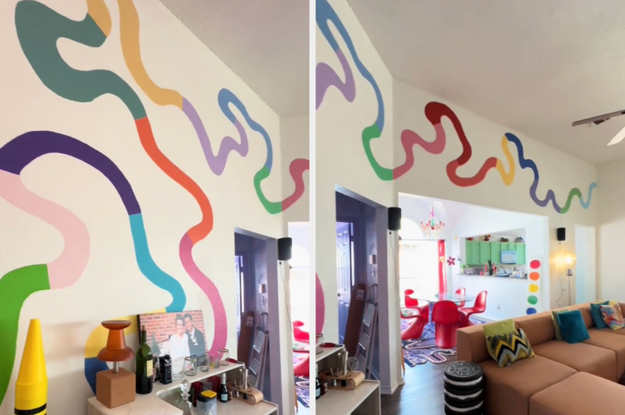 A vibrant mural with wavy lines with rainbow colors on a wall above a shelf with various items and a giant crayon sculpture
