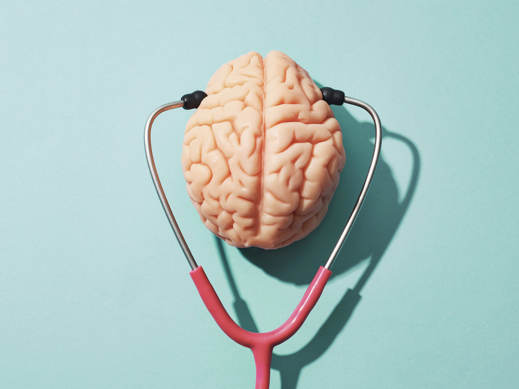 A stethoscope is wrapped around a model of a human brain on a plain background