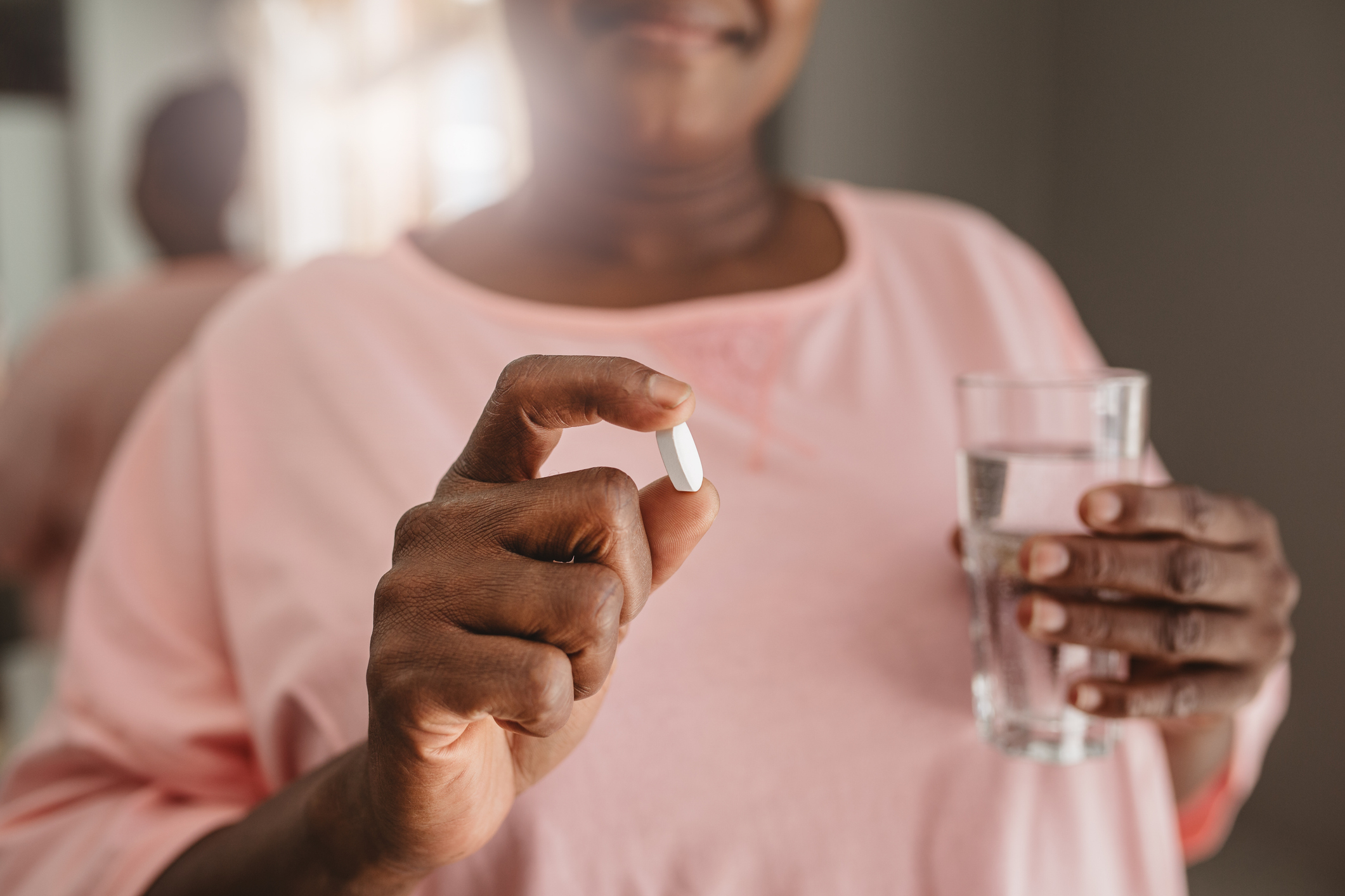 A person holding a pill in one hand and a glass of water in the other, ready to take the medication