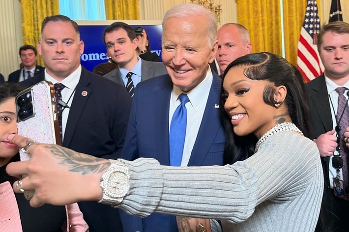 President with a guest smiling for a selfie amidst a group in a formal setting