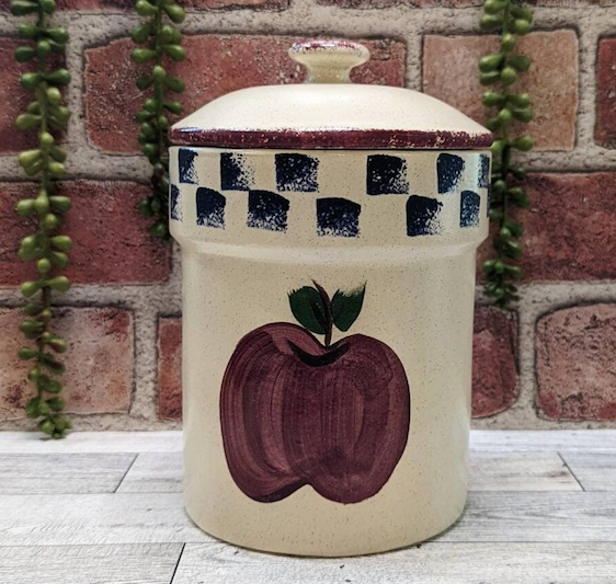 Vintage ceramic apple-designed kitchen canister on a counter with brick backdrop