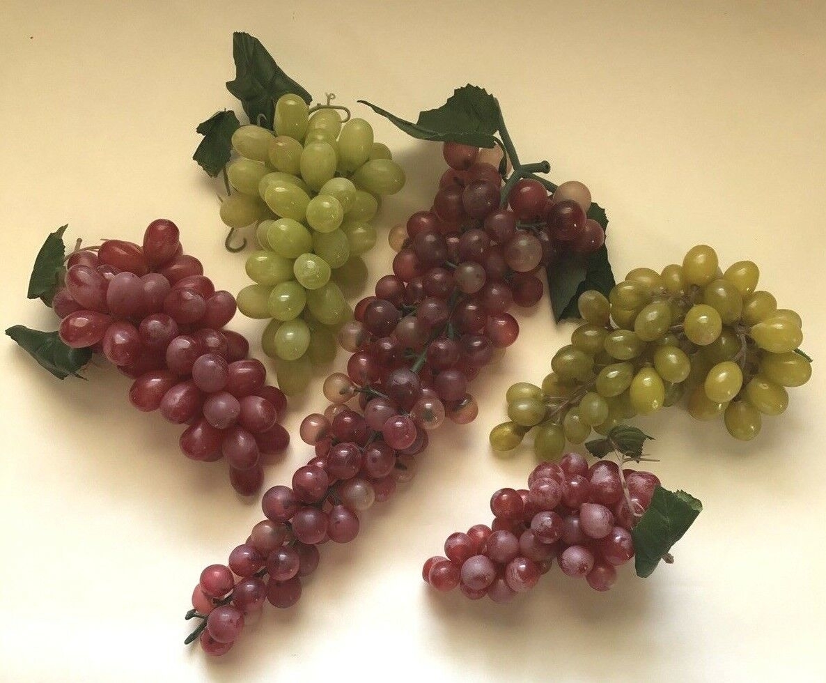 Four bunches of artificial grapes with varying shades arranged on a light surface